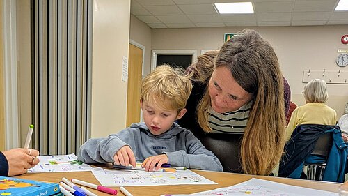 Vikki stood over a child doing some colouring in at a table
