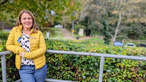 Vikki stood in front of a hedge leaning on a railing